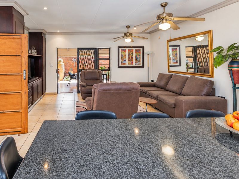 Open-plan living area featuring a granite kitchen island, tiled flooring, and direct access to an outdoor patio through a security-gated sliding door.