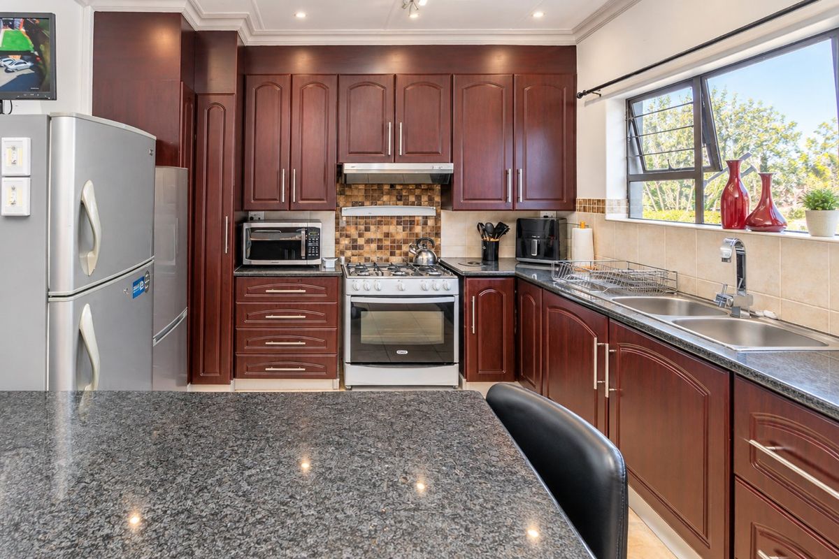 A well-maintained kitchen featuring dark wood cabinetry, granite countertops, a gas stove with extractor fan, and a mosaic tile backsplash.