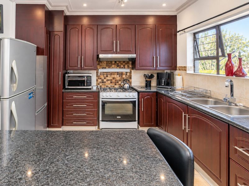 A well-maintained kitchen featuring dark wood cabinetry, granite countertops, a gas stove with extractor fan, and a mosaic tile backsplash.