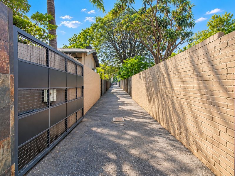 A secure, paved driveway entrance featuring high brick boundary walls and a modern metal security gate.