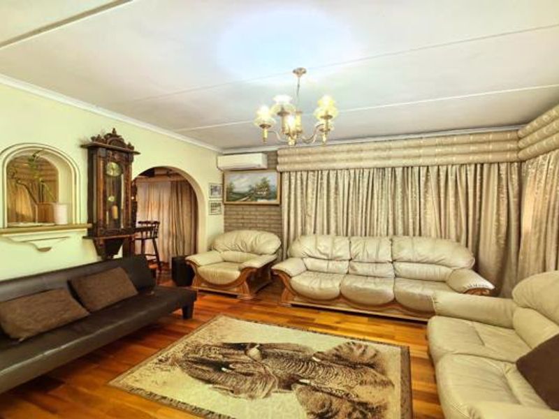 A spacious living room featuring hardwood flooring, a wall-mounted air conditioning unit, and an arched entryway leading to adjacent living spaces.