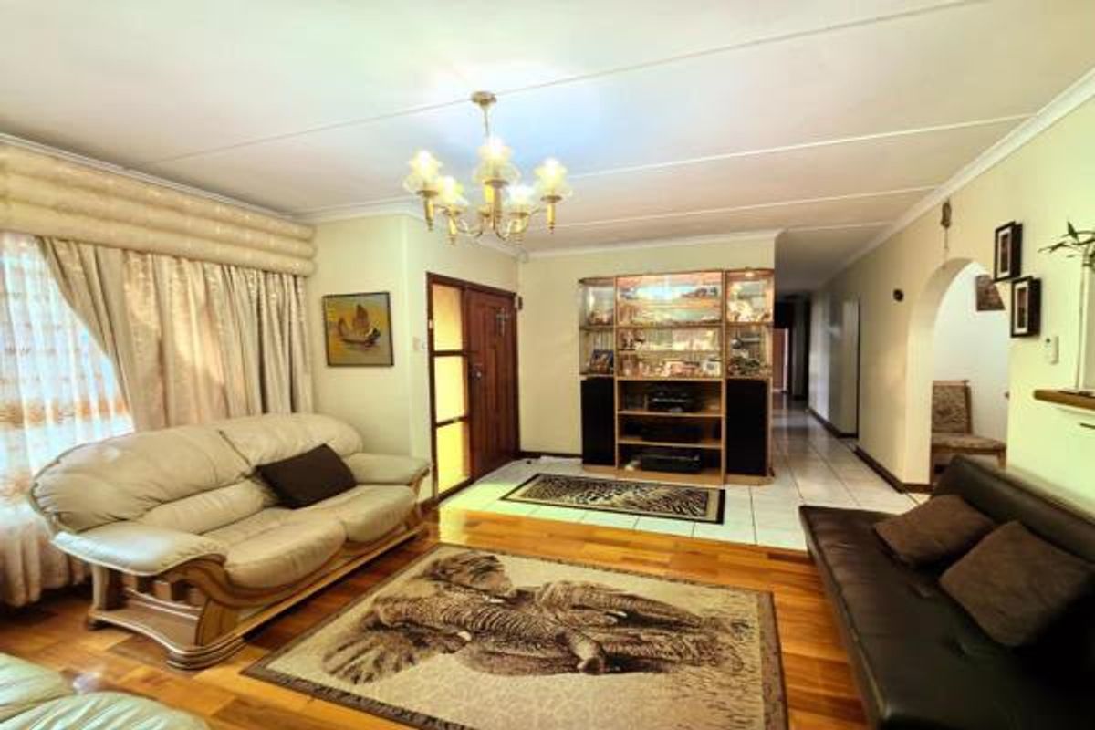 Spacious living room featuring a combination of tiled and wooden flooring, a built-in display cabinet, and a classic chandelier, leading to an arched hallway.