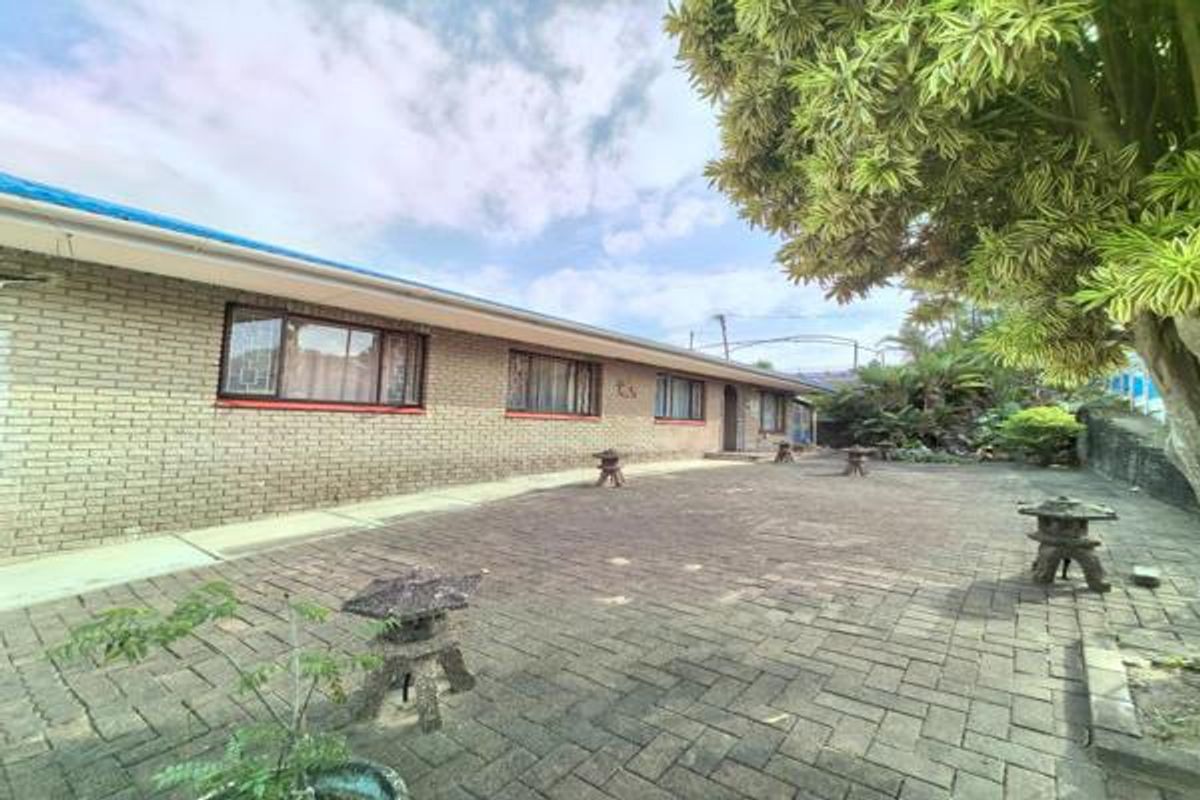 A spacious rear exterior view featuring a brick facade, paved courtyard area, and established garden surroundings.