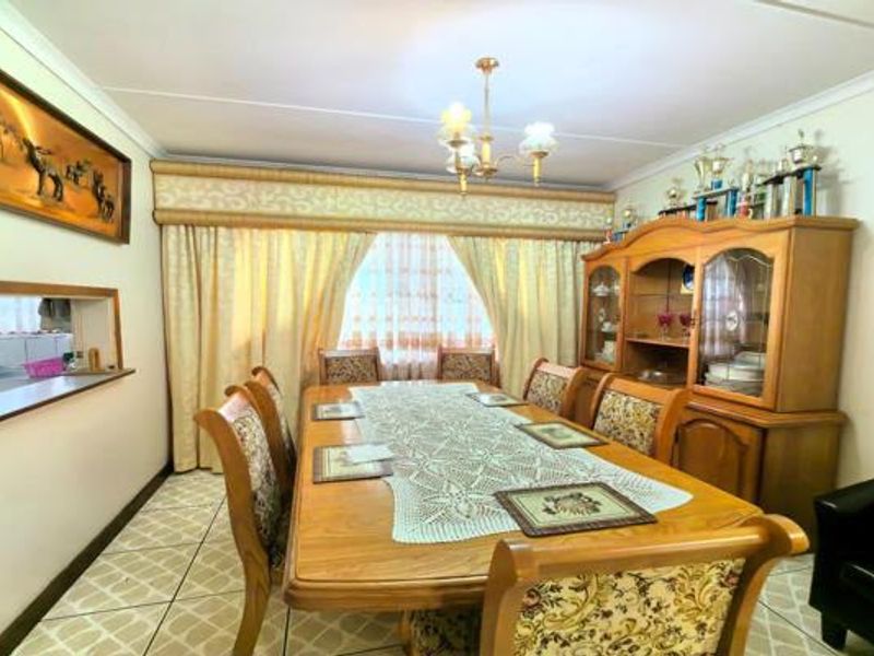 A traditional dining room featuring tiled flooring, a serving hatch to the kitchen, and a central chandelier, offering a functional space for family meals.