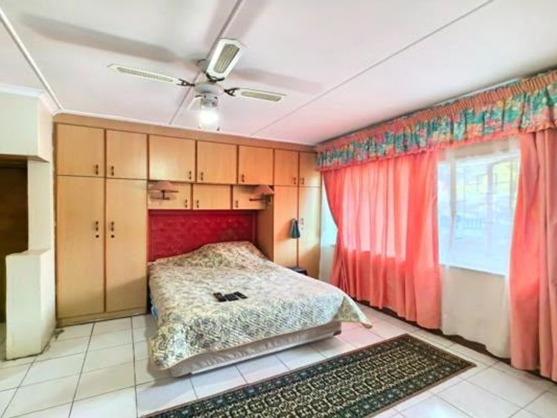 A bedroom featuring extensive built-in cabinetry, tiled flooring, and a ceiling fan, offering a functional layout with potential for modern updates.