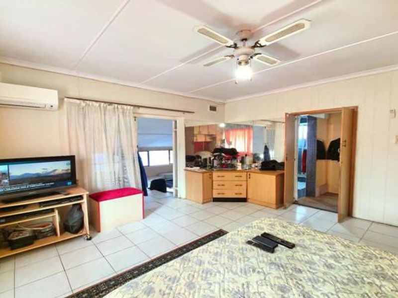 Spacious bedroom featuring tiled flooring, a ceiling fan, split-system air conditioning, and a built-in vanity area with mirrored walls.
