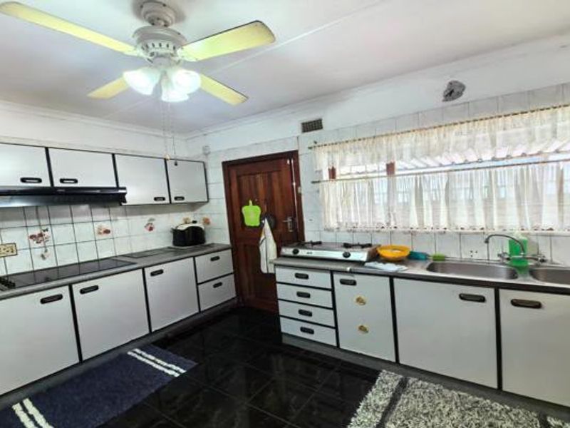 A functional kitchen featuring built-in cabinetry, a double sink, a hob with an extractor fan, and tiled flooring.