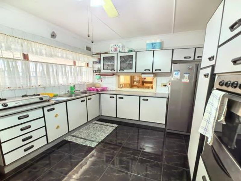 A functional kitchen featuring dated cabinetry, a gas hob, built-in oven, and dark tiled flooring with a pass-through window to the adjacent living area.