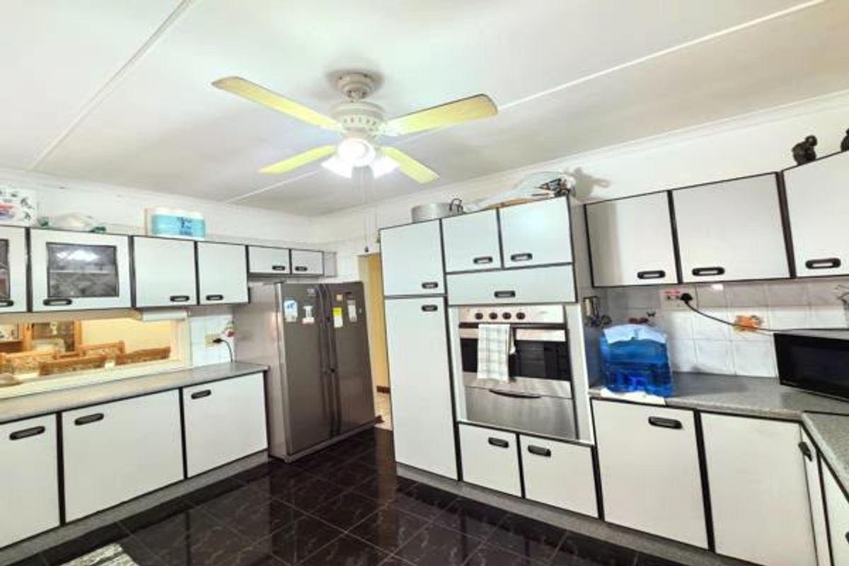 A functional kitchen featuring white built-in cabinetry, a built-in oven, dark tiled flooring, and a convenient pass-through window to the adjacent living area.
