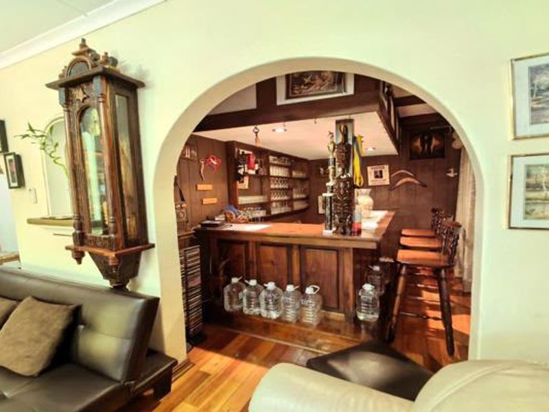 A dedicated home bar area featuring timber wall paneling, a built-in wooden counter, and hardwood flooring, accessed through a classic arched doorway.