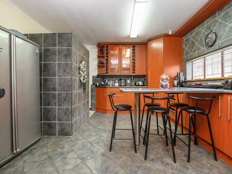 A functional kitchen featuring wood-toned cabinetry, a tiled splashback, and a central breakfast bar with integrated seating area.