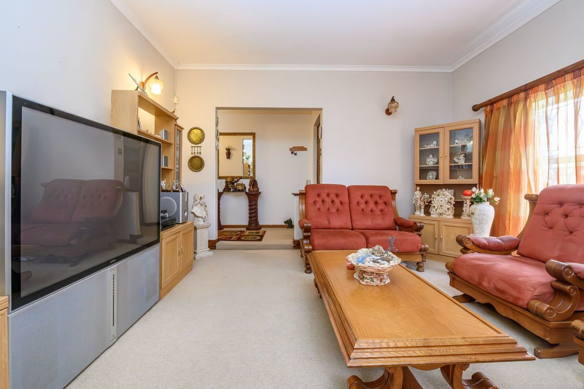 A spacious living room featuring neutral carpeting, cove cornicing, and wall-mounted lighting, offering a comfortable and functional layout.