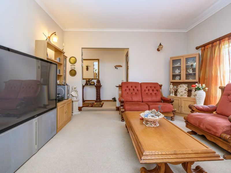 A spacious living room featuring neutral carpeting, cove cornicing, and wall-mounted lighting, offering a comfortable and functional layout.