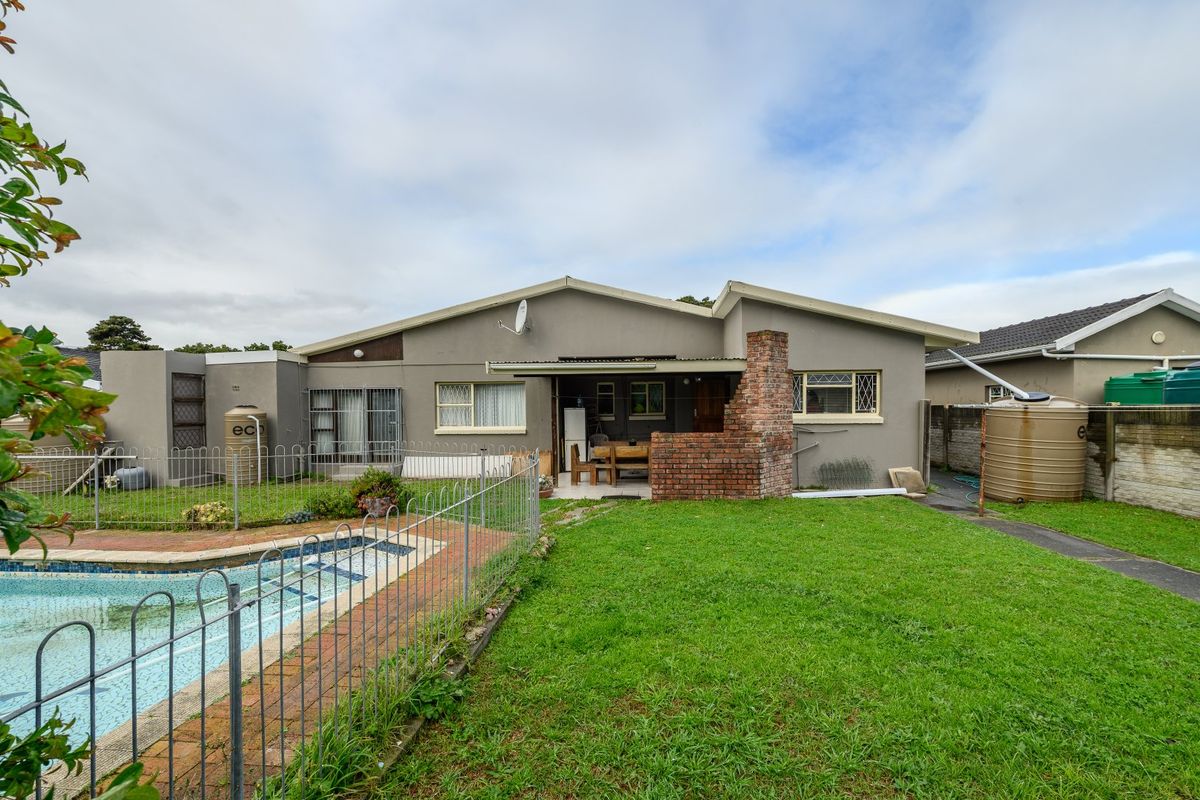 Rear view of the property featuring a swimming pool, brick chimney, covered patio area, and water storage tanks set within a grassed garden.