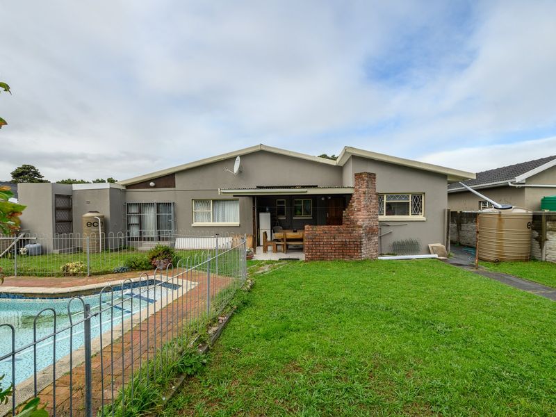 Rear view of the property featuring a swimming pool, brick chimney, covered patio area, and water storage tanks set within a grassed garden.