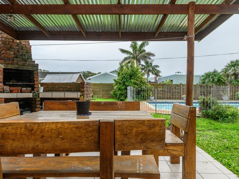 Covered outdoor patio featuring a built-in brick braai, timber pergola, and direct access to the garden and swimming pool area.