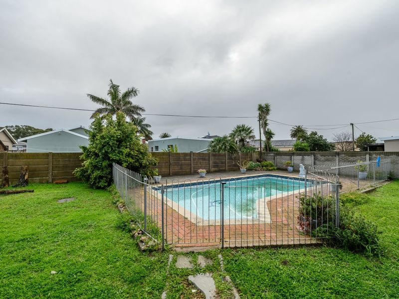 A backyard area featuring a swimming pool enclosed by metal fencing, set within a grassed garden with a perimeter boundary wall.