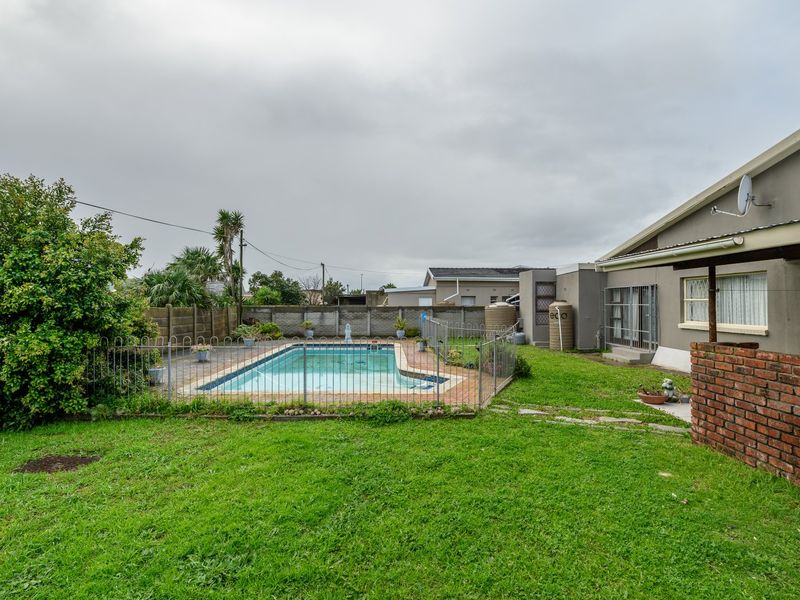Rear garden featuring a swimming pool with metal safety fencing, brick boundary walls, and water storage tanks.