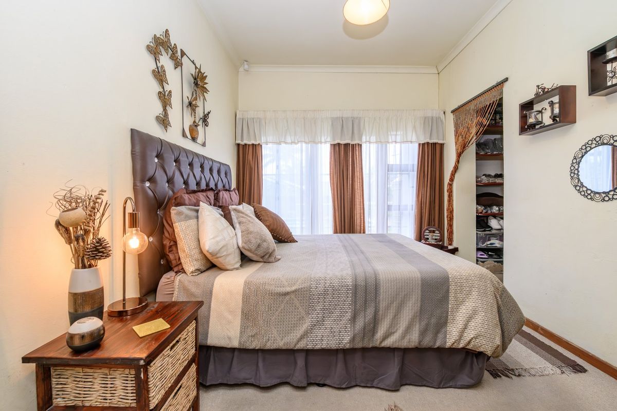 A cozy bedroom featuring carpet flooring, a built-in wardrobe, and large windows with curtains, providing a comfortable and functional living space.