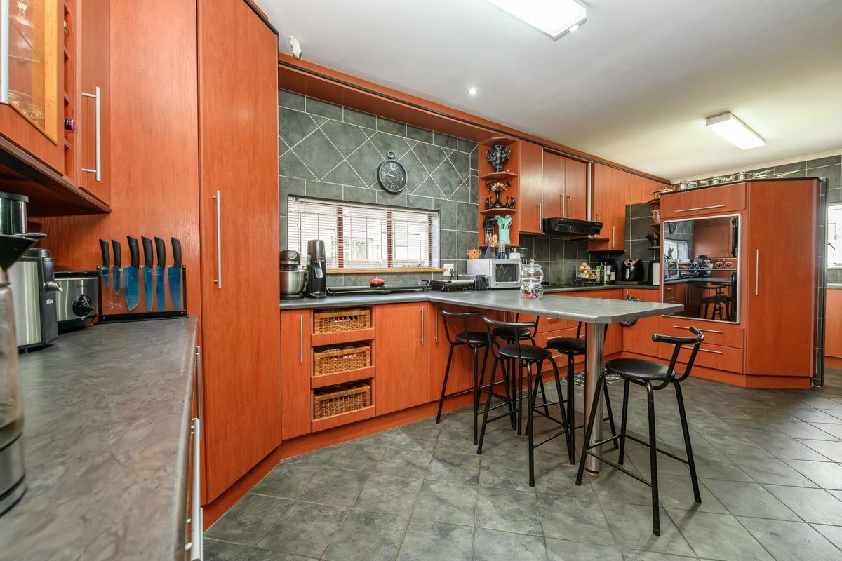 A functional kitchen featuring extensive wood-tone cabinetry, dark tiled backsplash, integrated oven, and a central breakfast bar with tiled flooring throughout.