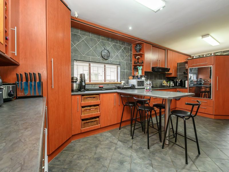 A functional kitchen featuring extensive wood-tone cabinetry, dark tiled backsplash, integrated oven, and a central breakfast bar with tiled flooring throughout.