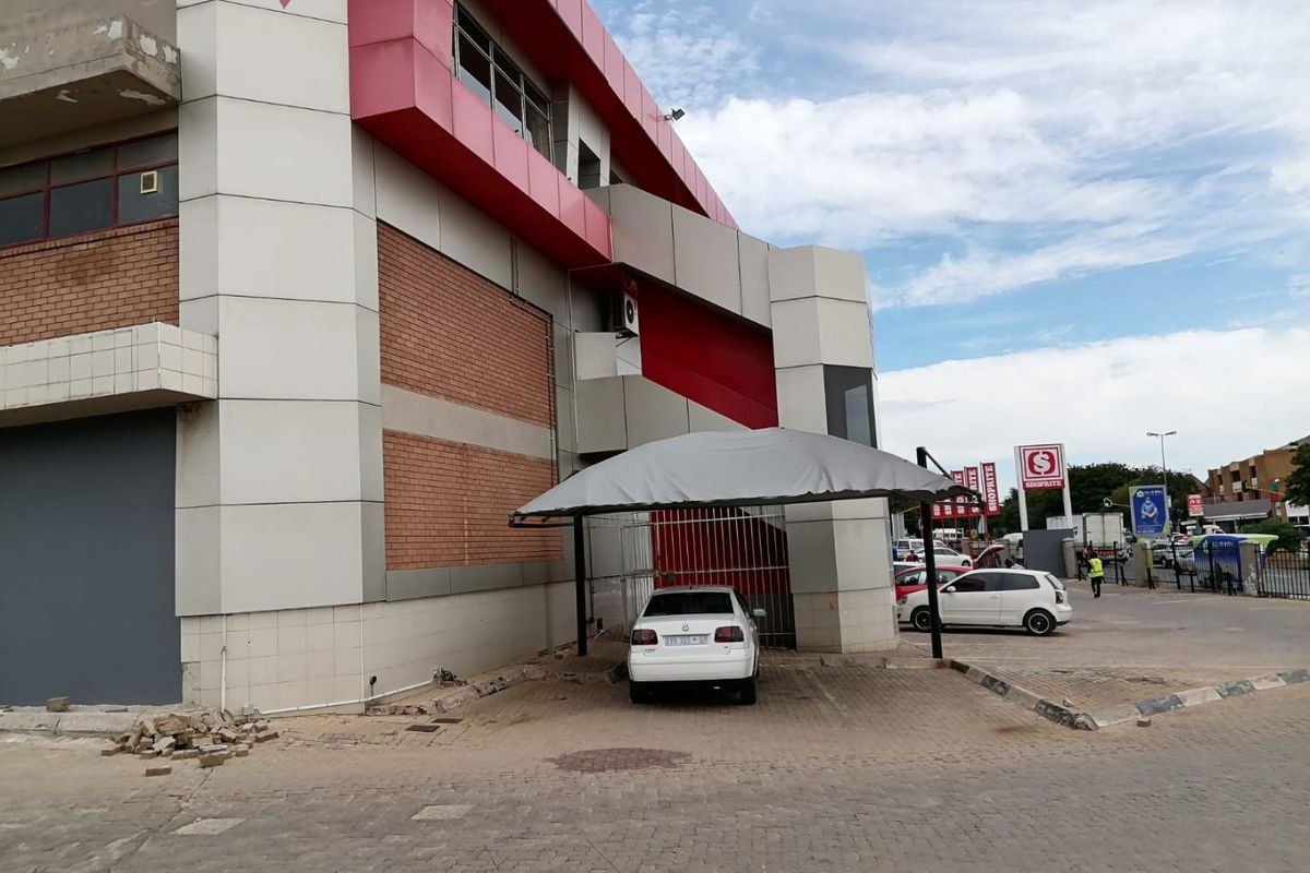 Exterior view of a commercial building featuring red and white cladding, brickwork accents, and a covered parking area with paved driveway.
