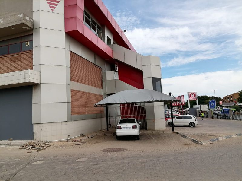 Exterior view of a commercial building featuring red and white cladding, brickwork accents, and a covered parking area with paved driveway.