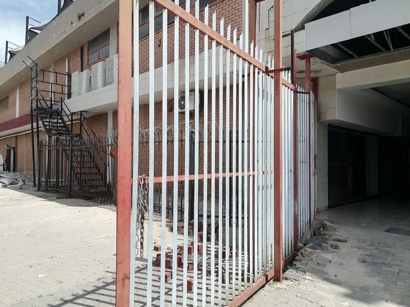 Rear exterior view of a commercial building featuring a metal security gate, external staircase, and brick facade with visible signs of wear and debris.