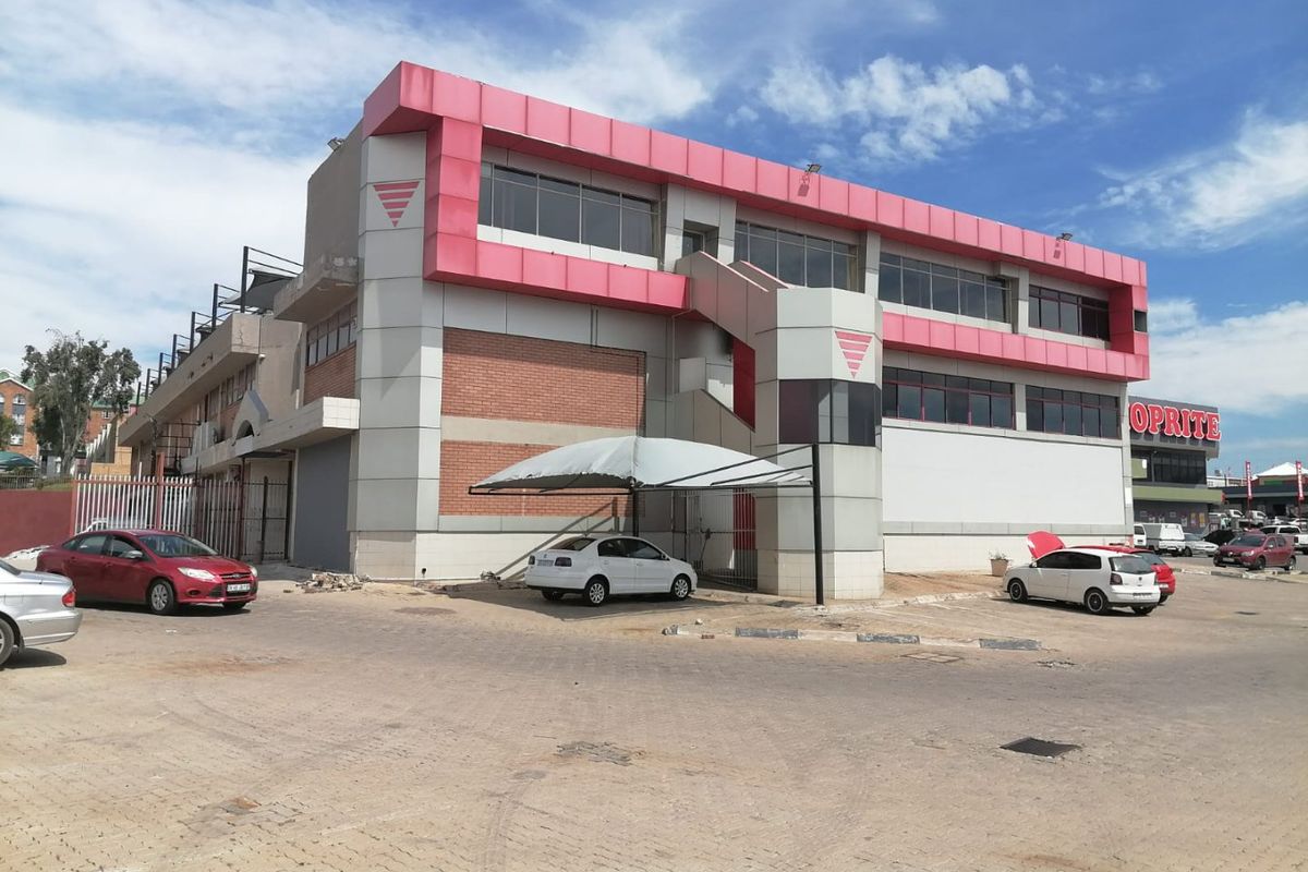 Commercial building exterior featuring metal cladding, brick accents, an external staircase, and a covered parking area in a paved lot.