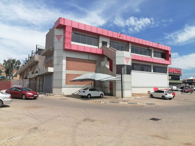 Commercial building exterior featuring metal cladding, brick accents, an external staircase, and a covered parking area in a paved lot.