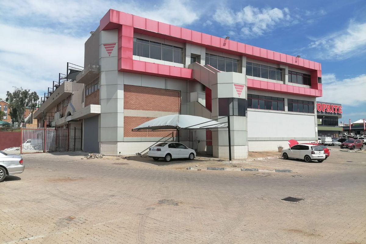 Commercial building exterior featuring a multi-level facade with metal cladding, brick accents, an external staircase, and a covered parking area.