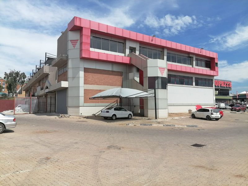 Commercial building exterior featuring a multi-level facade with metal cladding, brick accents, an external staircase, and a covered parking area.