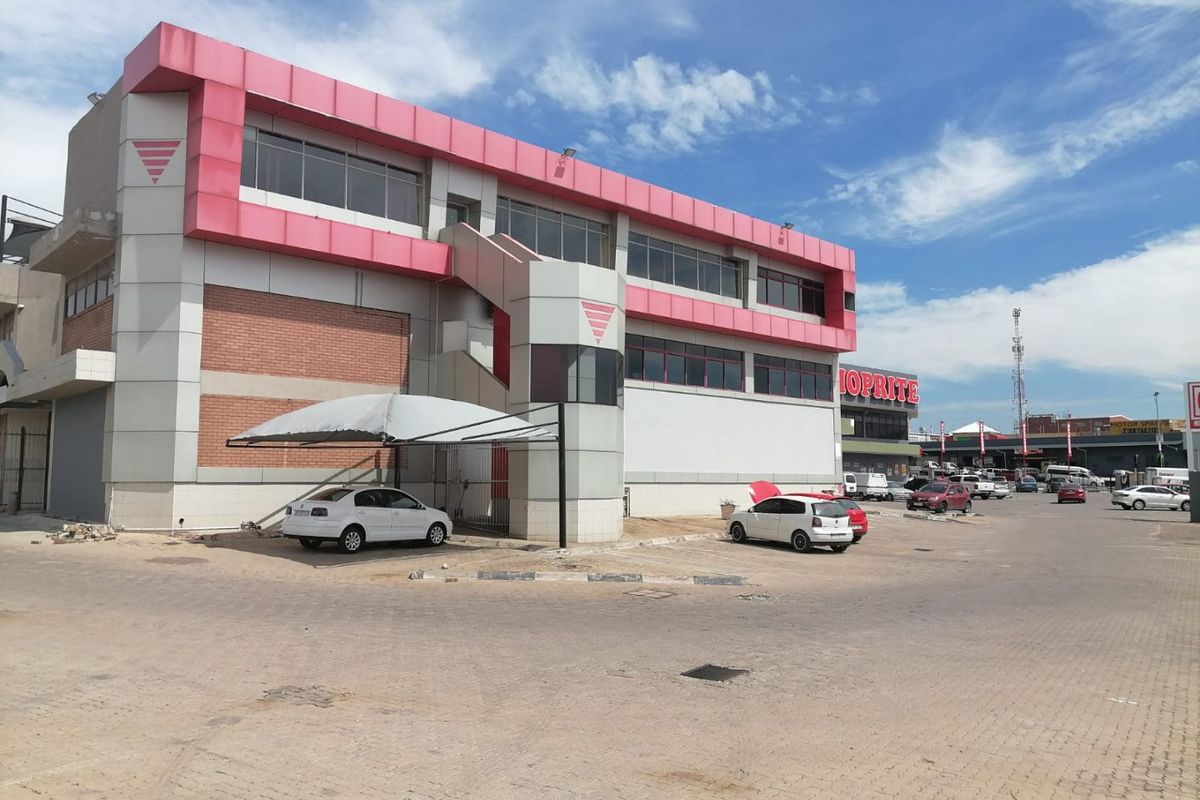 Exterior view of a multi-story commercial building featuring a paved parking area, carport, and prominent facade with external staircase access.