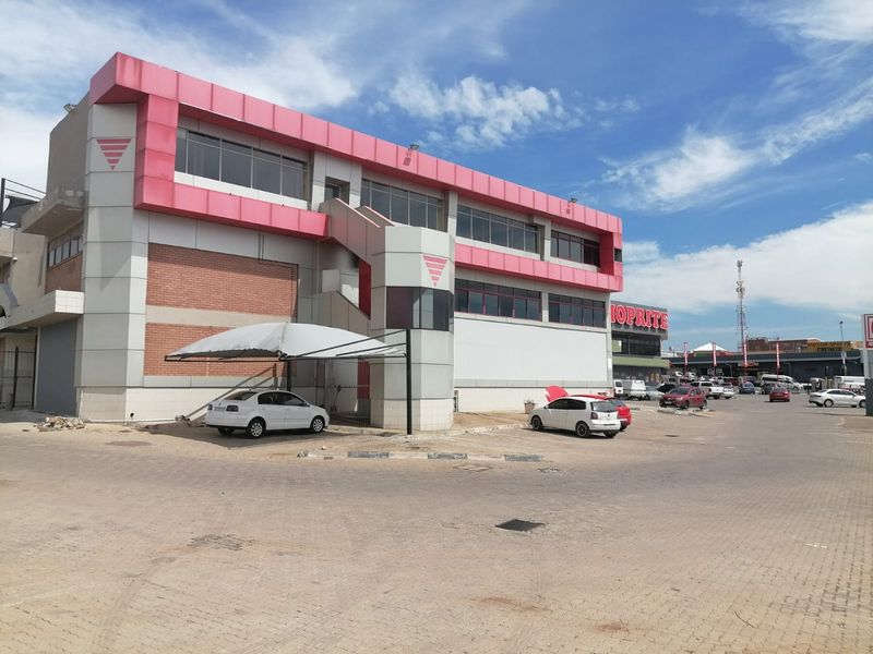 Exterior view of a multi-story commercial building featuring a paved parking area, carport, and prominent facade with external staircase access.