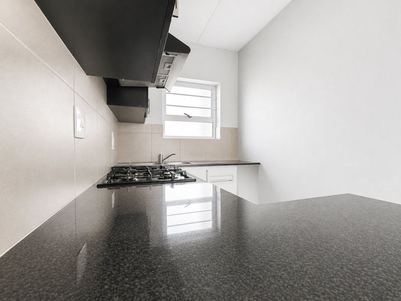 A clean, modern kitchen featuring dark granite countertops, a gas hob, an extractor fan, and neutral tiled backsplash with ample built-in cabinetry.