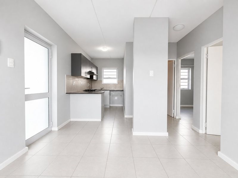 An open-plan living area featuring neutral tiled flooring, a modern kitchen with built-in cabinetry, and direct access to adjacent rooms.
