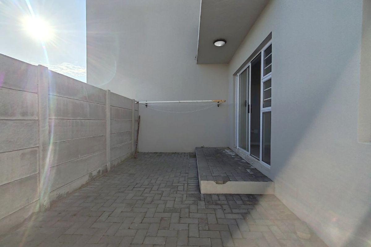 A private rear patio area featuring paved flooring, a sliding door entrance, and a wall-mounted clothesline, enclosed by a precast concrete boundary wall.