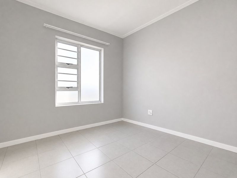 A bright, empty bedroom featuring neutral grey walls, tiled flooring, and a modern aluminium window frame, providing a clean canvas for personalization.
