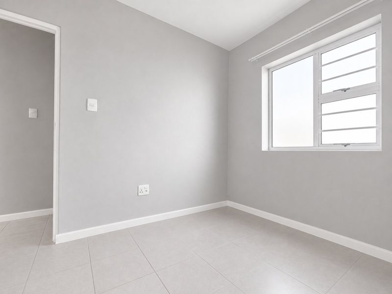 A clean, empty bedroom featuring neutral grey walls, tiled flooring, and an aluminium window with security bars.