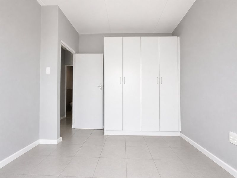 A clean, empty bedroom featuring neutral grey walls, tiled flooring, and white built-in cupboards, offering a versatile space ready for personalization.