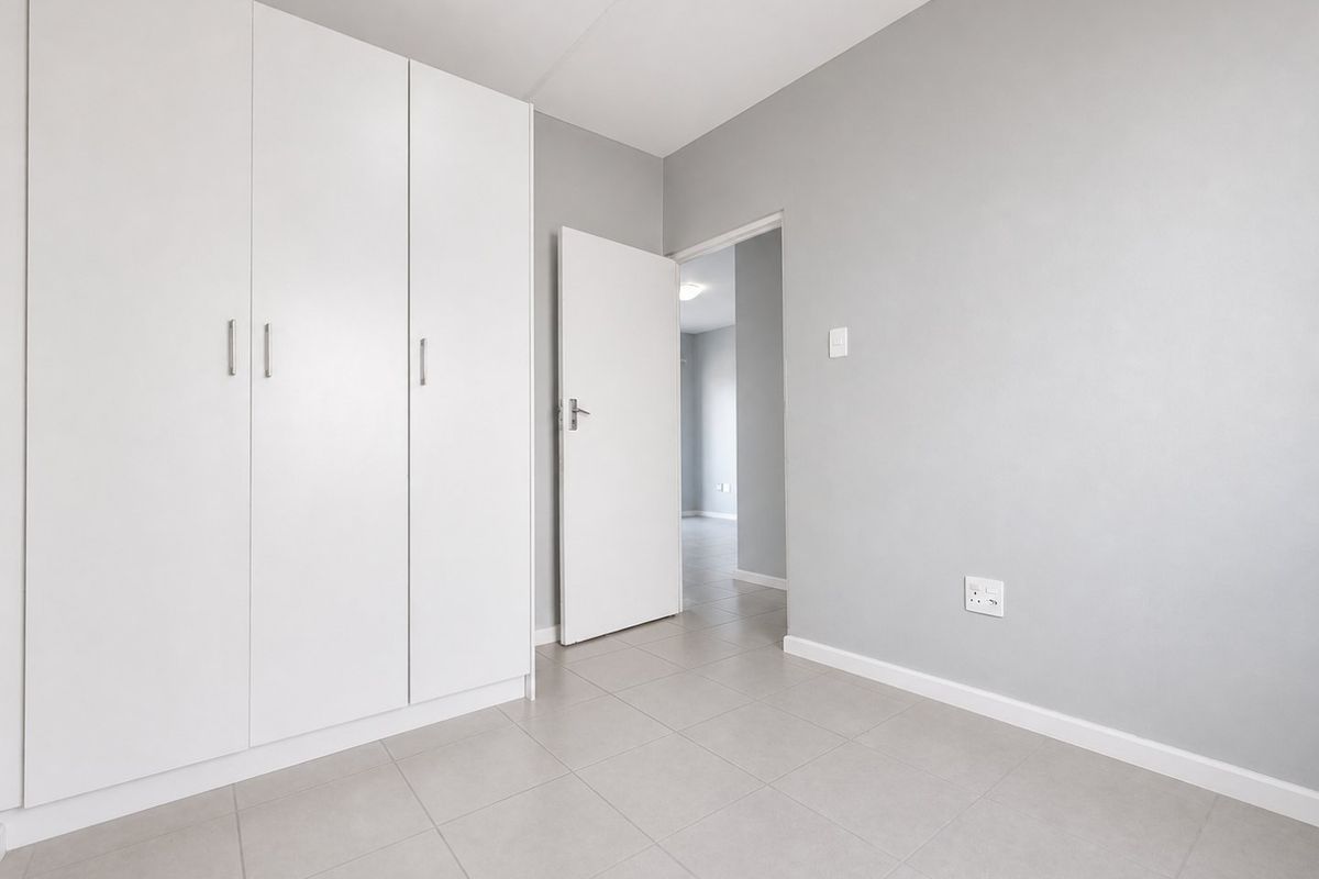 A clean, empty bedroom featuring neutral grey walls, tiled flooring, and built-in white cupboards, offering a versatile space ready for personalization.