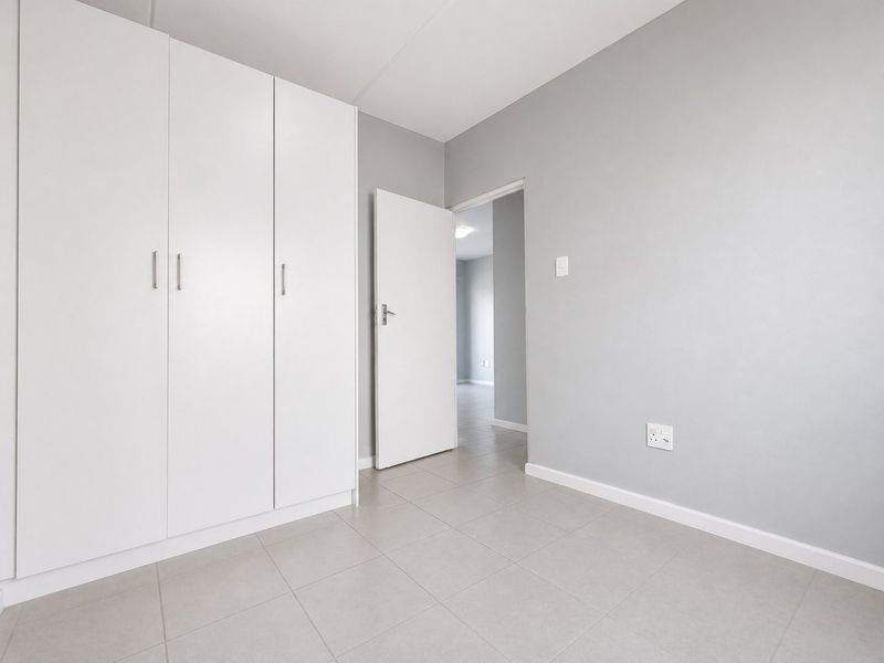 A clean, empty bedroom featuring neutral grey walls, tiled flooring, and built-in white cupboards, offering a versatile space ready for personalization.