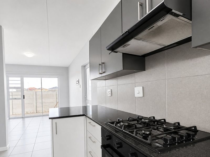 Modern kitchen featuring dark grey and white cabinetry, granite countertops, gas hob, built-in oven, and extractor fan, leading to an open living area.