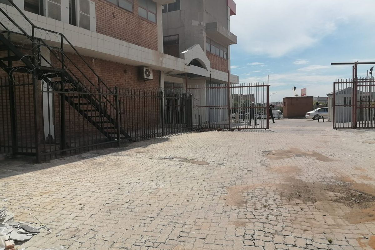 Commercial property exterior featuring a brick facade, paved driveway, metal security fencing with razor wire, and an external staircase.