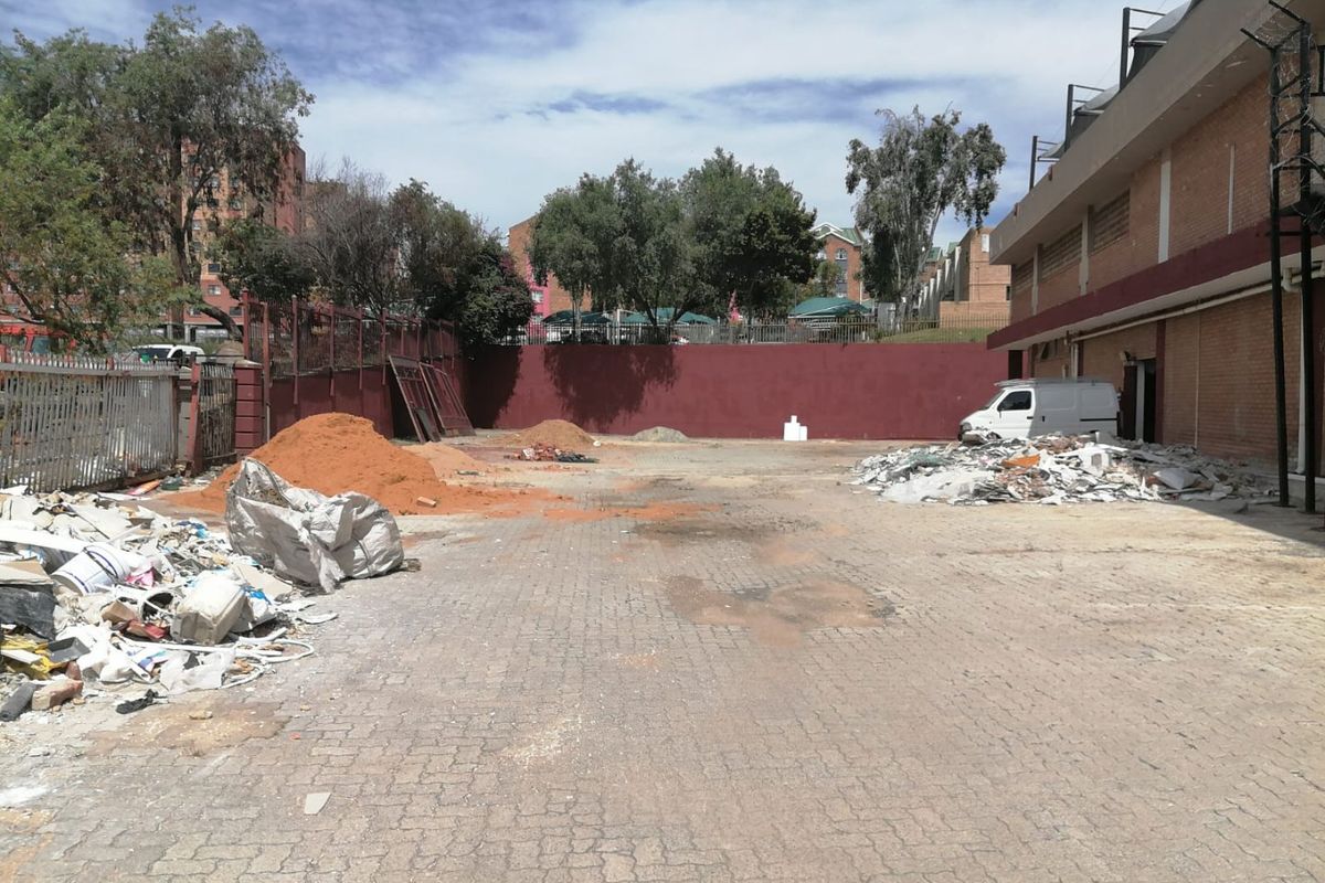 An expansive paved rear exterior area featuring perimeter walls and metal fencing, currently used for storage of construction materials and debris.