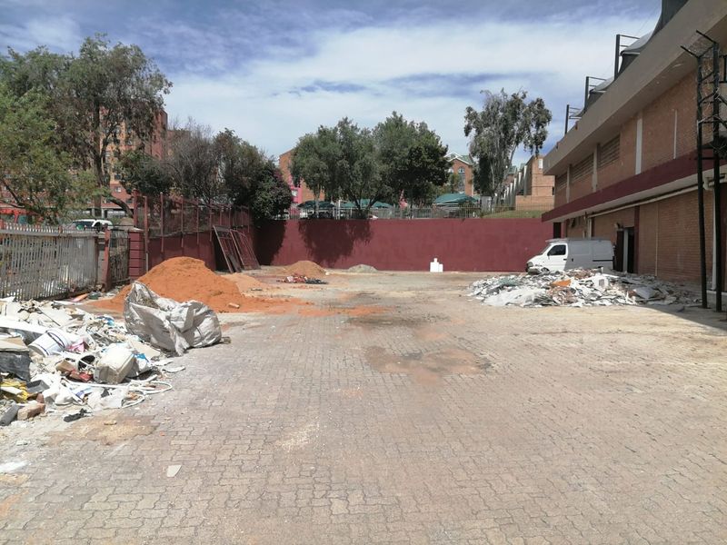 An expansive paved rear exterior area featuring perimeter walls and metal fencing, currently used for storage of construction materials and debris.