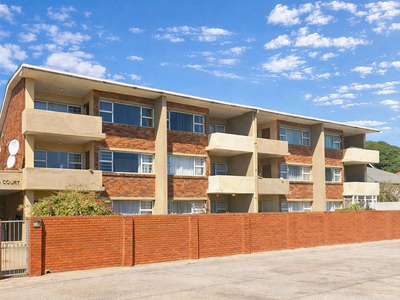 Exterior view of Elva Court apartment building featuring a brick facade, multiple balconies, and a secure brick boundary wall with gated access.