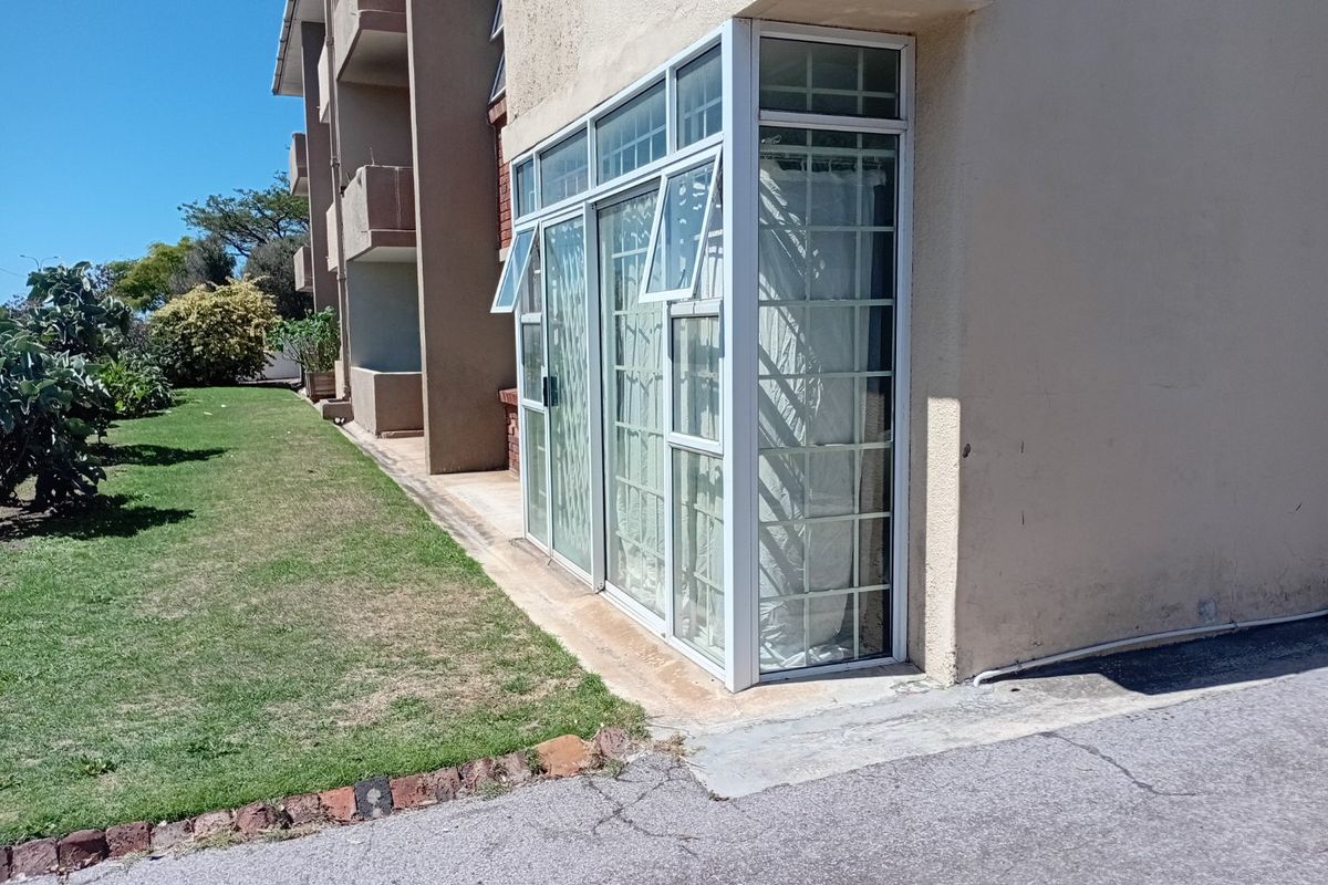 Rear exterior view of the apartment building featuring aluminium-framed windows with security bars and a paved walkway adjacent to the lawn.