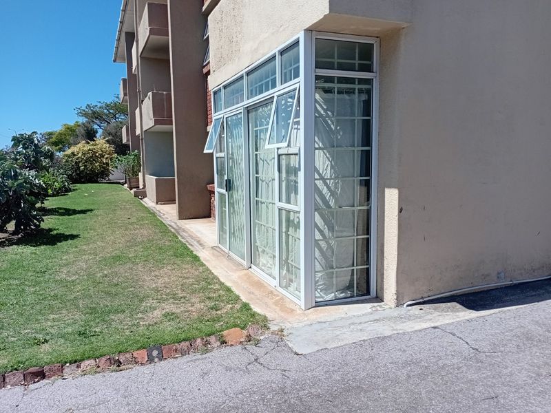 Rear exterior view of the apartment building featuring aluminium-framed windows with security bars and a paved walkway adjacent to the lawn.