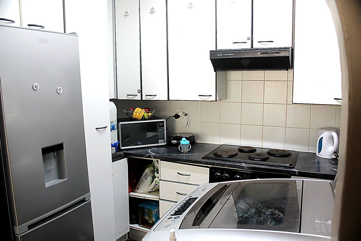 Compact kitchen featuring white cabinetry, dark laminate countertops, an electric hob with extractor fan, and tiled backsplash.